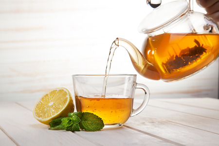 poured from a teapot cup of tea and lemon and mint on a wooden tableの写真素材