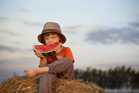 boy eating watermelon on a haystackの写真素材
