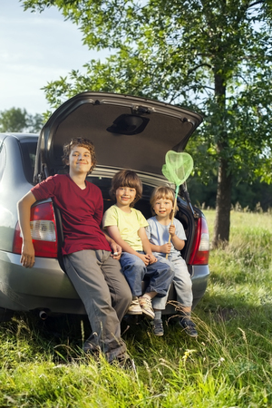 Three cheerful child sitting in the trunk of a car on natureの写真素材