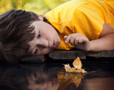 boy play with autumn leaf ship in water (focus on ship)の写真素材