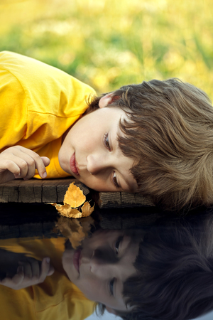 boy play with autumn leaf ship in water (focus on ship)の写真素材