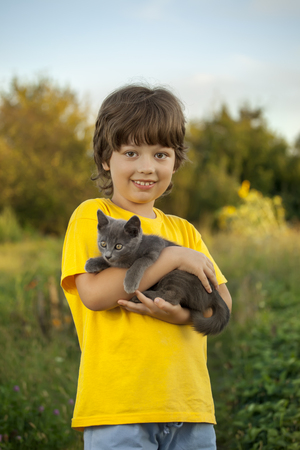 Happy kid with a kitten in her arms in natureの写真素材