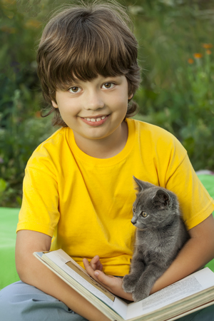 Boy reading book with kitten in the yard, child with pet reading magazine on the grass in the parkの写真素材