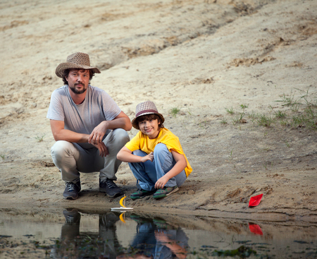 Father and son playing in the boats on the river bank, a family vacation on the lakeの写真素材