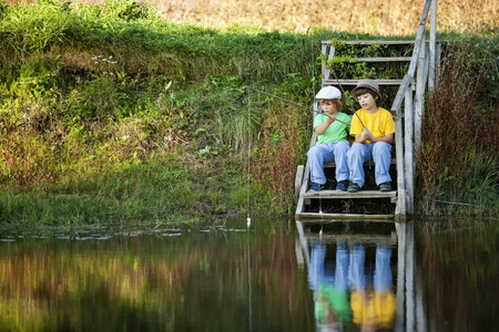 Happy boys go fishing on the river, Two children of the fisherman with a fishing rod on the shore of the lakeの写真素材