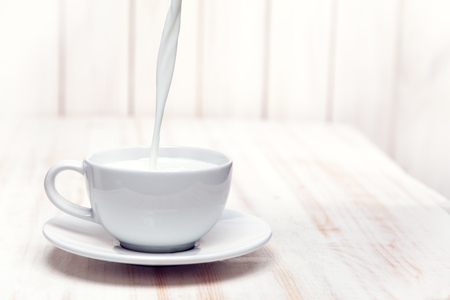Milk is poured into a cup white background wooden tableの写真素材