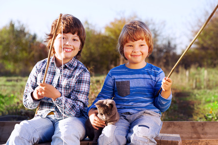 Happy boys go fishing on the river with pet, Two children and kitten of the fisherman with a fishing rod on the shore of the lakeの写真素材