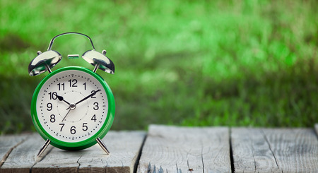 green clock on old wooden table in the summer garden on a sunny dayの写真素材