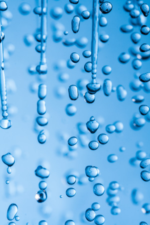 Falling water drops on blue background macro wet rainの写真素材