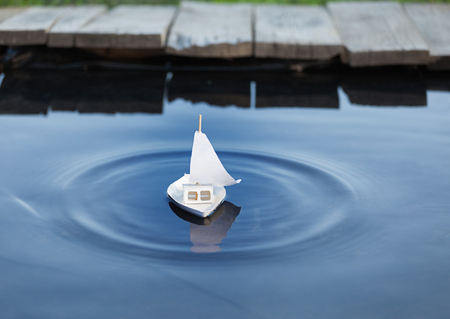 White toy boat at a pier in a pond in summerの写真素材