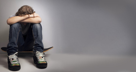 sad teenager sitting on skateboardの写真素材