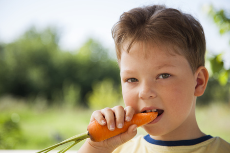 Happy boy biting the carrot, A child with a vegetable. Kid eating fresh carrotsの写真素材