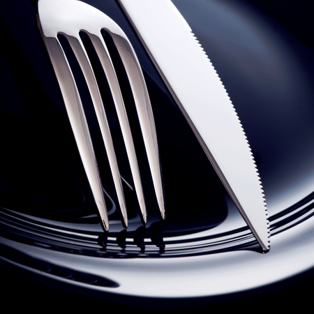 Empty plate with spoon, knife and fork on a black background.の写真素材