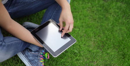 Beauty girl with tablet PC outdoors on green grassの写真素材