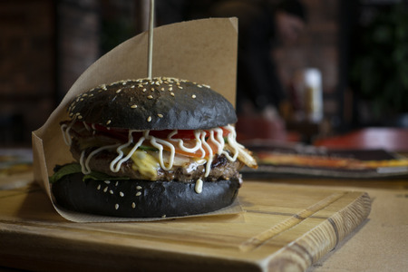 Fresh juicy tasty black burger with beef on wooden table in craft paper.の写真素材