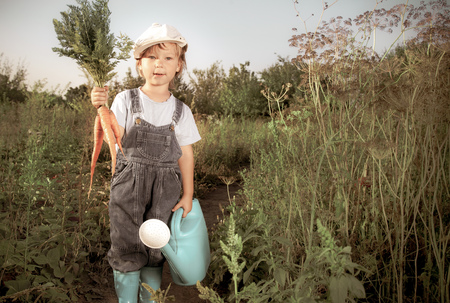 boy with a carrot and a watering can in the gardenの写真素材