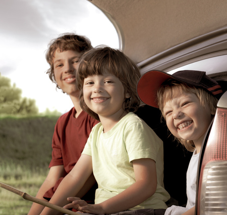 Three cheerful child sitting in the trunk of a car on natureの写真素材
