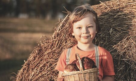 Boy with basket of buns in the background of haystacks in a field.