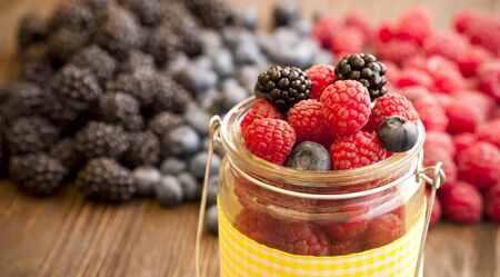 different berries (blueberries raspberries blackberries) in a basket on a wooden tableの写真素材