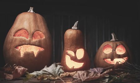 Jack o lanterns Halloween pumpkin face on wooden background and autumn leafsの写真素材
