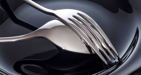 Empty plate with spoon and fork on a black background.