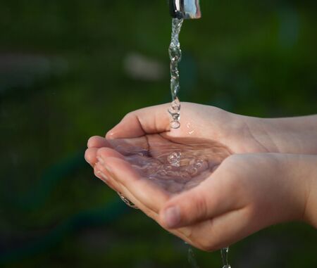 Boy washes his hand under the faucet in the garden