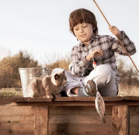 Happy boy go fishing on the river with pet, one children and kitten of the fisherman with a fishing rod on the shore of the lakeの写真素材