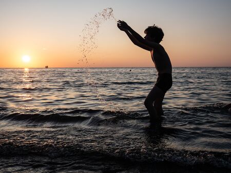 Boy splashing in sea with arms raised. Child playの写真素材