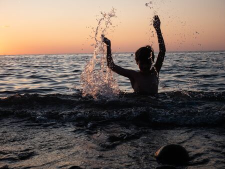 Boy splashing in sea with arms raised. Child playの写真素材