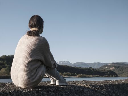 woman alone sitting on stone coast and looking at sea and mountanの写真素材