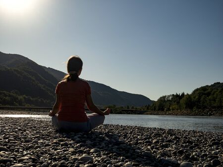 Young woman is practicing yoga in lotus pose at mountain lakeの写真素材