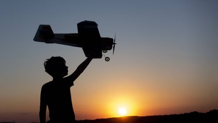 Happy Boy runs with a toy airplane on a field in the sunset light. Children play toy airplane. Teenager silhouette dreams of flying and becoming pilot.の写真素材