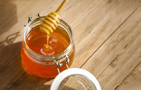Honey in glass jar on a wooden floor.
