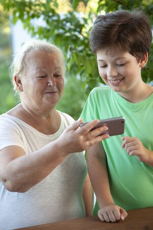 Boy using smartphone with grandma at home veranda.の写真素材