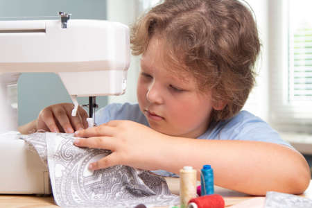Boy using sewing machine at home to make craftsの写真素材
