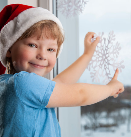 boy is sticking a snowflake near the winter window in the house Christmas Eve holiday tree.の写真素材