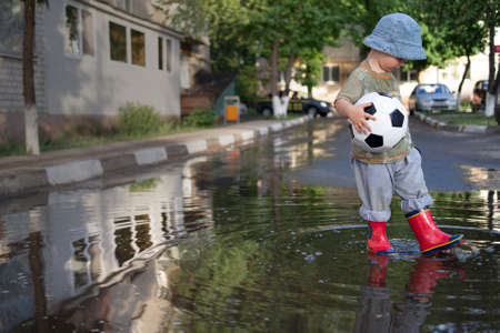 happy boy play in puddle with ball outdoorsの写真素材