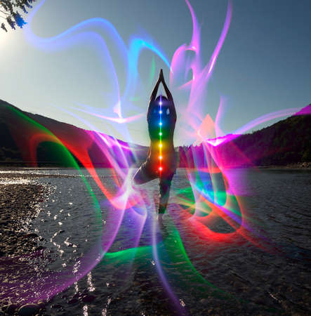 Silhouette of woman sits in a Upward Salute pose on beach sunset view, glowing seven all chakra....