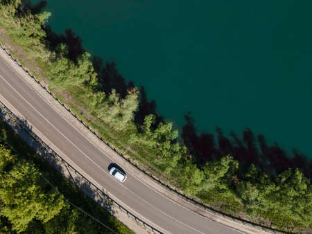 Aerial view of road between green summer forest and lakeの写真素材
