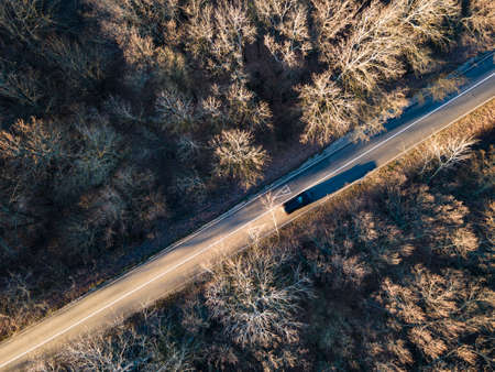 Aerial view of rural road with black car in winter forestの写真素材