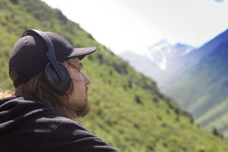 Young man in headphones listening to music in nature and at the mountain