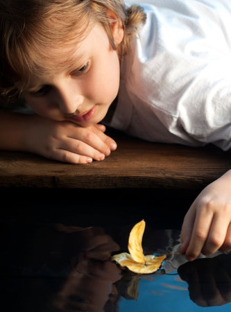 boy play with autumn leaf ship in water, children in park play with boat in riverの写真素材