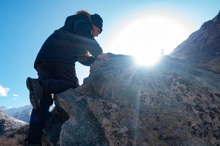 Boy climbs a rock against the snow winter mountains. Children rock climbing. Extreme hobby trains.