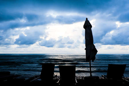 Silhouette of beach chairs and umbrella in tropical beach amid rainstorm background with copy space.の写真素材