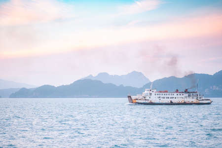 Beautiful sunset with mountain and ferry boat transporting passengers to island over horizon clam sea in evening background. Nature view of water transportation with golden light in summer vacation.の写真素材