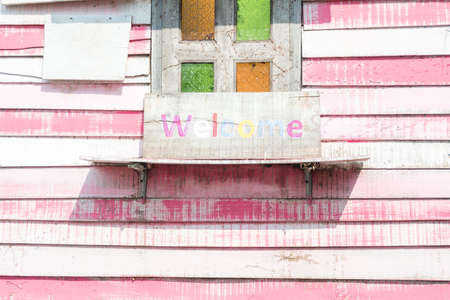 Vintage wood shelf with painted on old and rustic wooden board welcome sign with window frame on pink wood texture and background with drop shadow.の写真素材