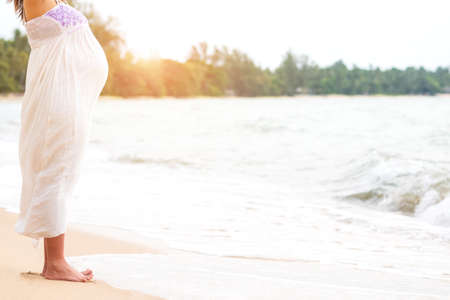 Happy and beautiful Pregnant woman wear white maternity dress standing on beach and stretching with blurred tropical sea background in summer time. Pregnancy traveling vacation in summer for relax.の写真素材