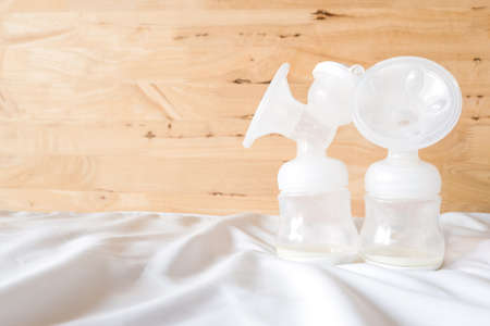 Bottles of automatic breast pump with fresh mother breast milk for baby on white bed sheet and wooden background in bedroom. Breast pump and store in refrigerator help breast milk stay fresh longer.の写真素材
