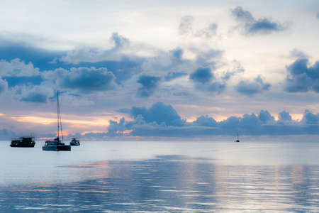 Soft focus of boats in the middle of sea suface amidst dark clouds at sunset.の写真素材