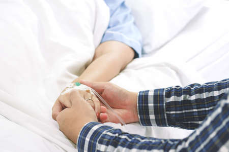 Man hand holding woman patient hand receiving saline solution by intravenous injection on bed in hospital for reassuring and encouragement wife. Medical treatment, healthcare, family and love concept.の写真素材